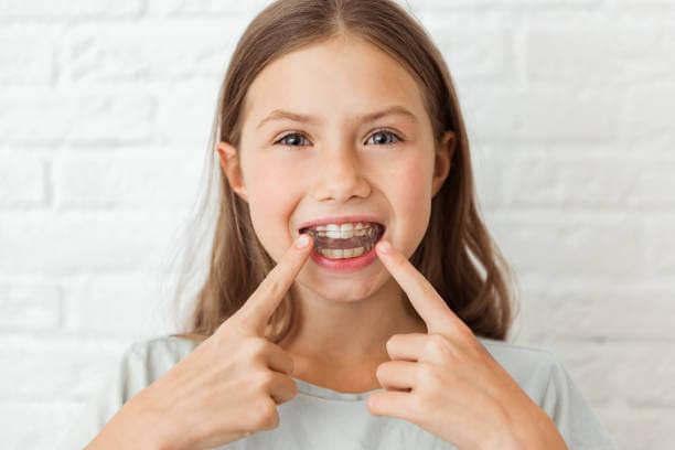 child smiling while wearing clear retainers, showcasing their orthodontic progress