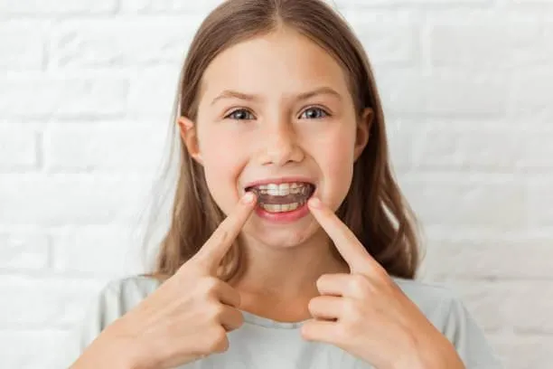 child smiling while wearing clear retainers, showcasing their orthodontic progress
